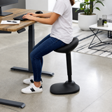 Woman perching on the Ergox EA-R15-BK wobble stool while typing at a standing desk